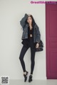 A woman standing in front of a red door wearing black leggings and a denim jacket.