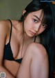 A woman with long black hair sitting on a bed.