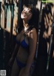 A woman in a blue bikini leaning against a fence.